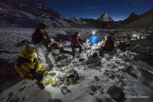 The picture shows the participants to the expedition having the dinner in the base camp, outside the tents, during the cold night of the Corner glacier